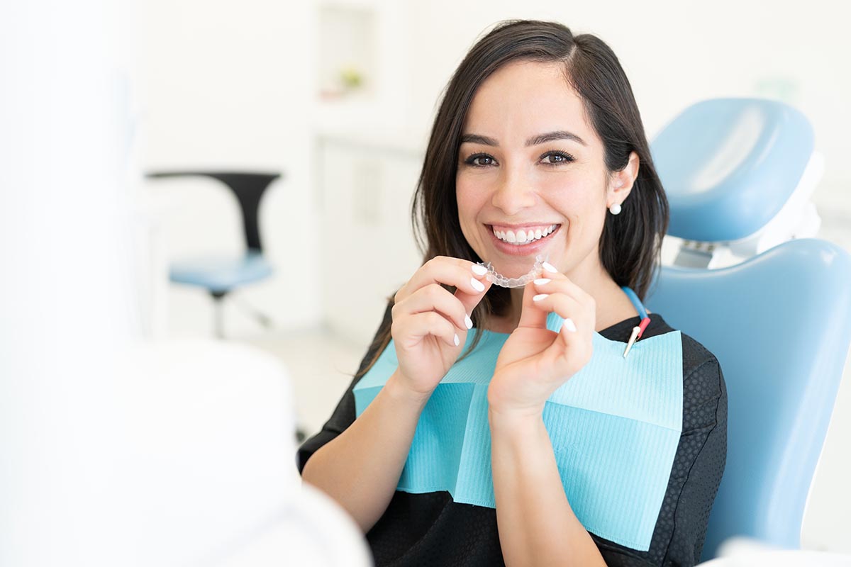 Smiling beautiful Caucasian mid adult woman holding invisible orthodontic retainer